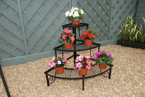 Three-tiered metal plant stand with potted plants against a wooden fence.